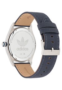 Hodinky Adidas s puzdrom z nehrdzavejúcej ocele, námorníckym látkovým a koženým remienkom, striebornými doplnkami a puzdrom s vygravírovaným logom. Vodotesnosť 5ATM.
