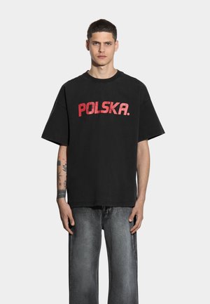 Czarna bawełniana koszulka z krótkim rękawem i szerokim krojem. Posiada wyraźny napis "POLSKA" w kolorze czerwonym na piersi. Teksturowana tkanina i prosty design.