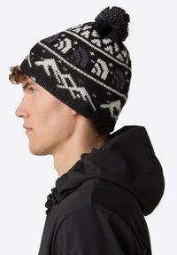 Berretto a maglia bianco e nero con pom-pom, caratterizzato da un motivo geometrico. Ha una vestibilità aderente ed è realizzato in filato testurizzato.