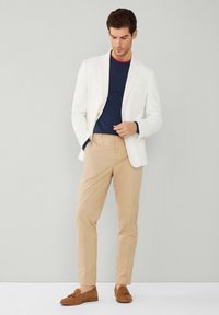 Witte blazer, marineblauw T-shirt met rode rand, kaki broek en bruine suède instappers. Glad materiaal, getailleerde pasvorm en minimalistisch ontwerp.
