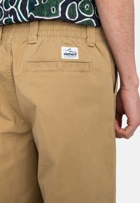 Khaki šortky s elastickým pásom, so zadnou vreckom a značkovou nášivkou. Tkanina má hladkú, pevnou štruktúru.