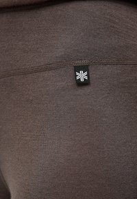 Bruine stretchy leggings met een gladde textuur, voorzien van een zwart label met een wit logo op de zijnaad. Eenvoudig, nauwsluitend ontwerp.