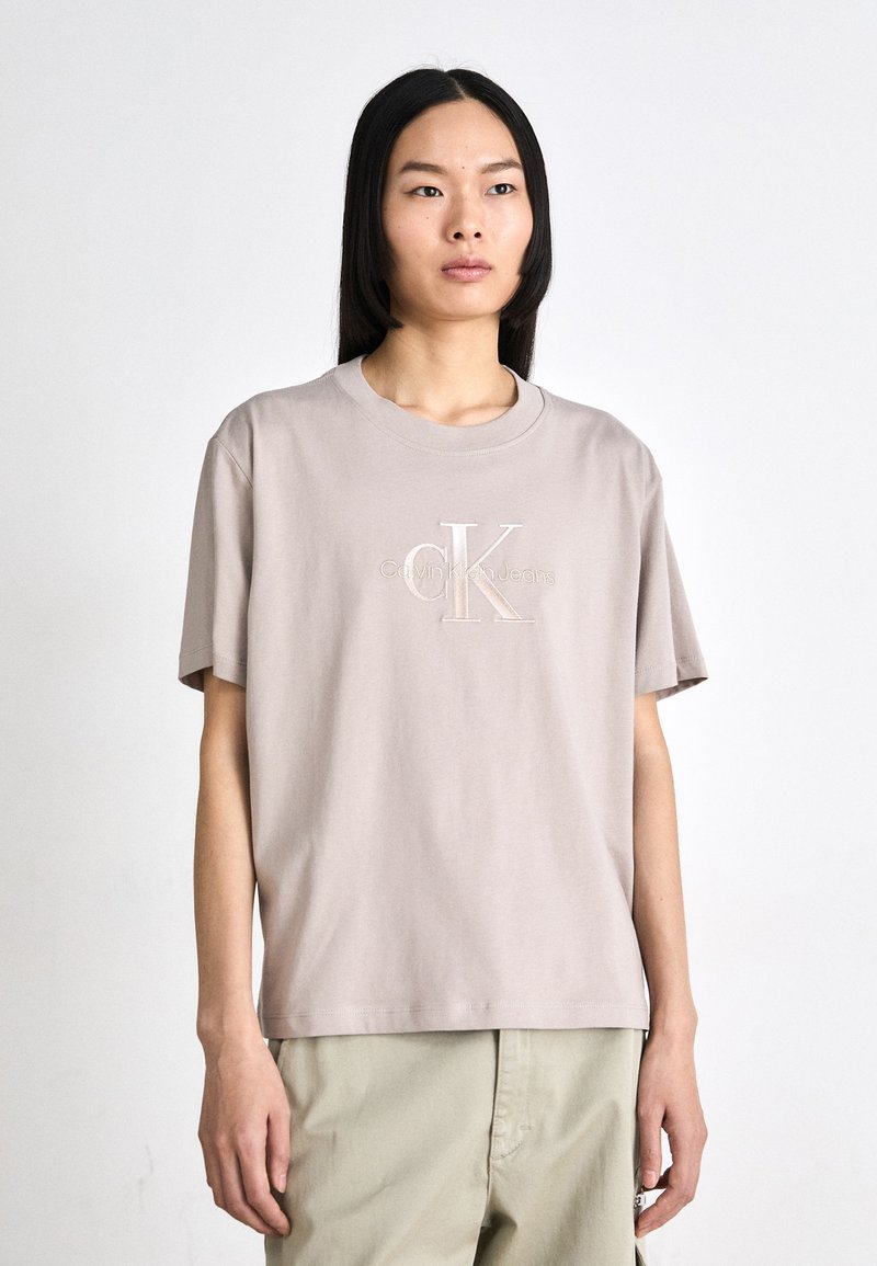 Šviesiai kreminės spalvos medvilnės marškinėliai su apvaliomis iškirptėmis ir trumpomis rankovėmis. Papuošti siuvinėtų "CK" logotipu ir subtiliu tekstu "Calvin Klein Jeans".