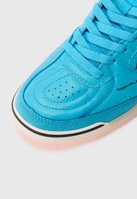 Zapatilla de piel azul con superficie texturizada, collar acolchado y puntera perforada. Suela blanca y negra con acentos transparentes en color rosa.