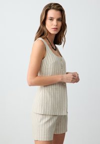 Linnenmix-outfit met een mouwloze, lichtbeige top met verticale zwarte strepen, voor knopen en bijpassende shorts.