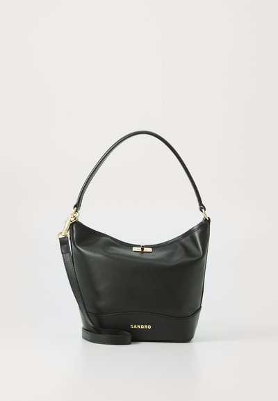 Sac à main en cuir noir avec un design incurvé, métallisation dorée et une bandoulière amovible. Arbore un logo sur le bas de l'avant et une texture lisse.
