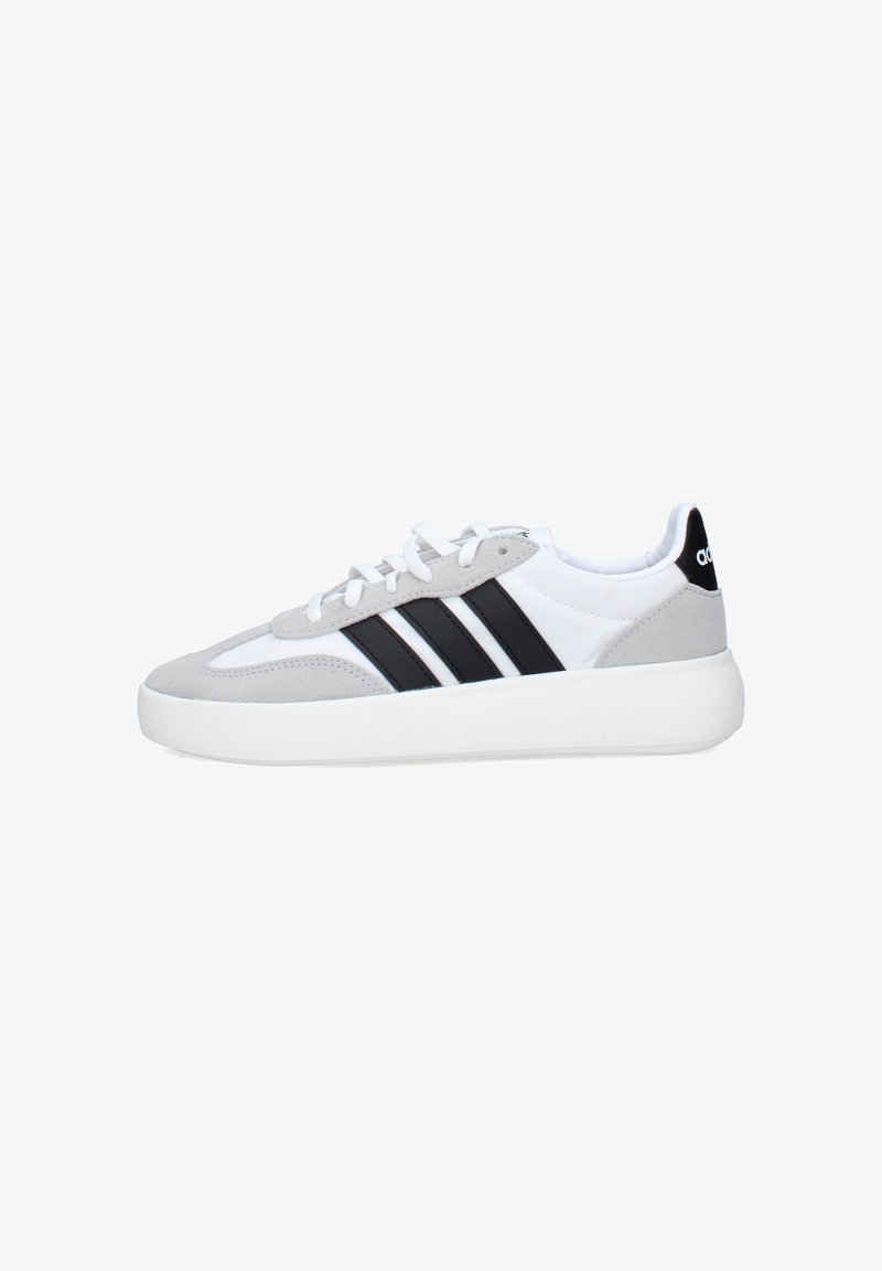 Baskets basses blanches et grises avec des bandes noires, une semelle épaisse blanche et un passant de talon noir avec un logo blanc, vue de côté.