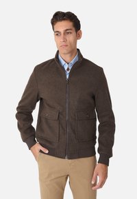 Giacca marrone con zip realizzata in tessuto testurizzato, caratterizzata da un colletto alto, due tasche frontali e polsini a coste.