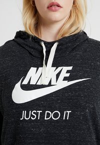 Sudadera negra con el logo blanco de Nike y el texto "JUST DO IT". Presenta una capucha con cordones, un corte relajado y una tela texturizada.