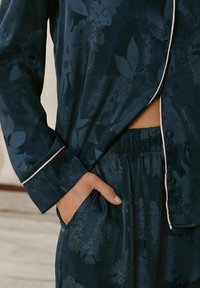 Navy floral pajama set with satin finish; features light pink piping on cuffs and waistband; includes a pocket on the side.