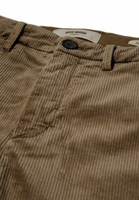 Pantaloni di velluto a coste marroni con righe verticali, dotati di chiusura a bottone nero e etichetta del marchio. Tessuto liscio e vestibilità tailored.