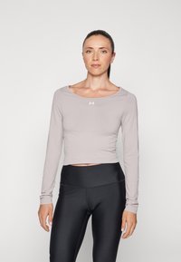 Svijetlosivi dugi rukavi skraćeni top s okruglim izrezom i suptilnim šavovima, uparen s crnim tajicama visokog struka. Prikazan Under Armour logo.