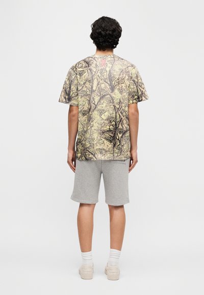 Κοντομάνικη μπλούζα με καμουφλάζ μοτίβο σε αποχρώσεις καμηλό και πράσινο, συνδυασμένη με γκρι  σορτς. Διαθέτει άνετη εφαρμογή και απαλό ύφασμα. Πιθανή λεπτομέρεια με λογότυπο.