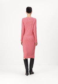 Langärmliges Midi-Kleid mit einem strukturierten roten Muster; figurbetonte Silhouette, ergänzt durch hohe schwarze glänzende Stiefel.