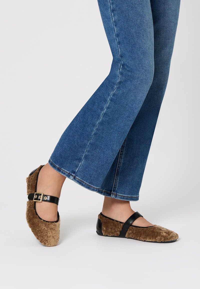 Scarpe slip-on marroni e pelose con dettagli in pelle nera e punta arrotondata. Le scarpe presentano una texture morbida e un design a profilo basso.