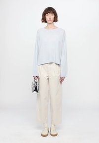 Hele sinises toonides lühendatud kudum, millel on sooniktekstuur, koos beežide nööridega laia jalaga pükstega. Modell hoiab käes väikest hõbedast käekotti ja kannab kreemikaid tossusid.