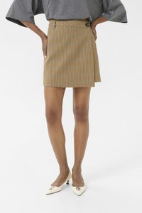 Une mini-jupe vichy jaune et marron avec un détail de boutons à l'avant et un léger design croisé, associée à des talons blancs pointus avec des accents argentés.
