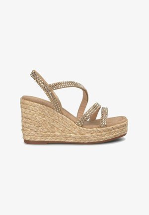 Sandale à talon compensé avec une base en jute tressé, des brides beiges ornées de petites pierres précieuses et une semelle intérieure douce. La vue de côté montre un design ouvert.