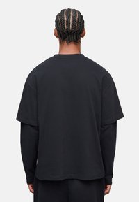 Schwarzes, übergroßes T-Shirt mit kurzen Ärmeln und lässiger Passform, aus weichem Stoff gefertigt und mit einem runden Halsausschnitt; keine sichtbaren Marken oder Muster.