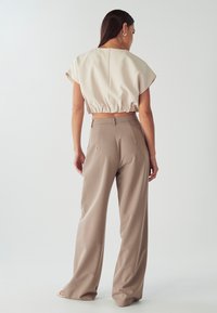 Top beige corto con maniche a cappuccio e orlo elastico abbinato a pantaloni taupe a vita alta e gamba larga; tessuto morbido, con dettagli minimali.