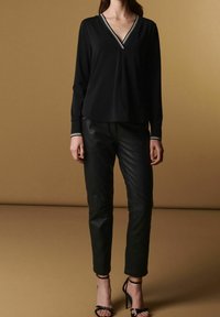 Maglietta nera a maniche lunghe con scollatura a V, caratterizzata da dettagli a righe bianche sul colletto e sui polsini. Abbinata a pantaloni in pelle nera a sigaretta e tacchi a strappo.