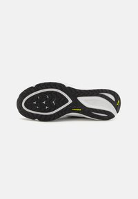 Suela de goma negra con un patrón de agarre texturizado, que presenta una entresuela blanca y un pequeño logo amarillo. En general, el diseño es funcional y deportivo.