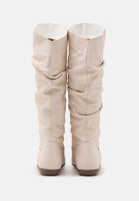 Botas de cuero beige hasta la rodilla con una textura suave y recogida y punta redondeada. Los empeines presentan un diseño caído y un interior liso.