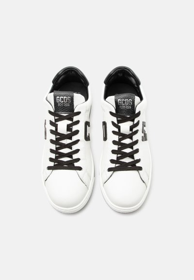 Λευκά δερμάτινα sneakers με μαύρα κορδόνια, μαύρο πέλμα πτέρνας και μαύρες λεπτομέρειες με το λογότυπο "GCDS" στα πλευρά και στη γλώσσα.