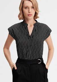 Blouse à manches courtes rayée noir et blanc avec un col, dotée d'une patte de boutonnage et d'une coupe décontractée, associée à un pantalon noir taille haute.
