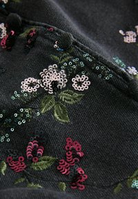 Must mustril, mille lilledega, mis on broderitud roosa, valge ja rohelise värviga, kaetud erinevate värvide sädelustega ja tekstureeritud pinnaga.