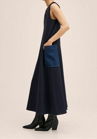 Vestido sin mangas de color navy con un corte holgado, que presenta un bolsillo de denim. Combinado con botas de tobillo negras de tacón. Textura de tela suave.