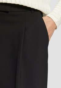 Schwarze, taillierte Hosen mit einer glatten Textur, die über Seitentaschen und eine schmale Taille verfügen. Das Material wirkt strukturiert und leicht.