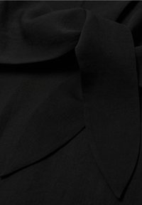 Gros plan sur un tissu noir avec des plis visibles et une texture subtile, mettant en valeur un matériau doux et lisse superposé en formes qui se chevauchent.