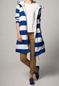 Vattentålig lång kappa med växlande blå och vita ränder, med dragkedja fram, huva och resårmidja. Matchad med beigefärgade byxor.