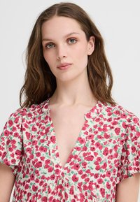 Floral dress in lightweight fabric with a v-neck and short sleeves, featuring a pink and green floral pattern against a white background.