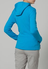 Blauwe hoodie met een gladde textuur, aansluitend ontwerp en een ritszak op de taille, gecombineerd met lichtgrijze broek.