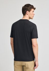 T-shirt di cotone nero con maniche corte e scollatura a girocollo, vista dal retro. Presenta una texture liscia e un orlo dritto.