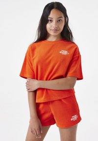 Felroze handdoekenstof set met een losvallende top met korte mouwen en bijpassende shorts, beide met een opvallend wit logo detail.