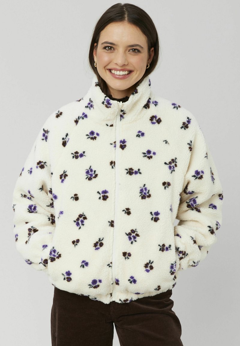 Veste en polaire crème avec imprimé floral violet et marron, col haut, fermeture éclair, et poignets et ourlet élastiques pour un ajustement parfait.