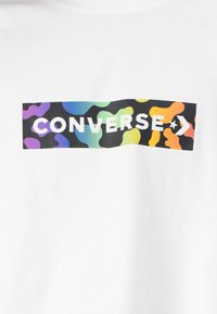 Hvit T-skjorte med en stor svart rektangulær logo med fargerike abstrakte former og ordet "CONVERSE" i fete hvite bokstaver.