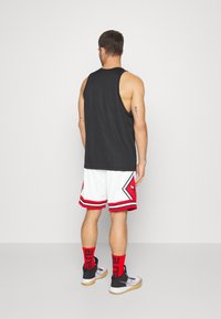 Camiseta sin mangas negra, pantalones cortos blancos con detalles en rojo y negro, medias hasta la rodilla en negro y rojo, y zapatillas negras con suela de goma.
