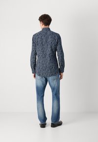 Navy floral button-up shirt with a slim fit, long sleeves, and a curved hem, paired with light blue jeans and black shoes.