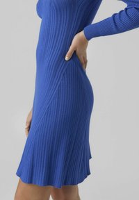 Robe en tricot côtelé bleu profond, présentant une silhouette ajustée, des manches longues et un ourlet évasé. Texture lisse avec des lignes verticales.