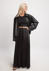 Črna jakna iz umetnega usnja s skrajšano zasnovo, v kombinaciji s črnim rebrastim crop topom in dolgo črno satensko krilo. Gladka tekstura, sproščen kroj.