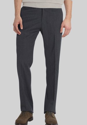 Donkergrijze broek gemaakt van een zachte stof, met een rechte snit, minimale plooien en een subtiel verticaal patroon. Gecombineerd met bruine schoenen.