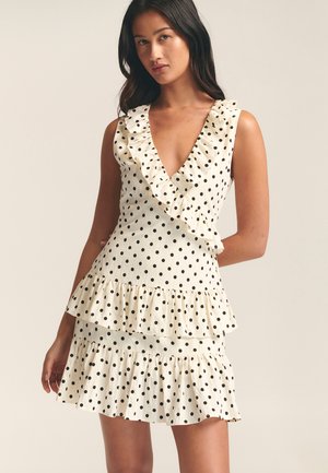 Polka dot dress in cream with a deep V-neckline, ruffled accents, and layered frills at the hem. Made from a lightweight fabric.