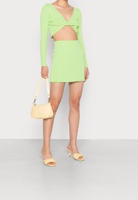 Grön, ribbadt kort top med långa ärmar och djup V-ringning, matchat med en mini kjol med scalloped nederkant. Gul handväska och sandaler.