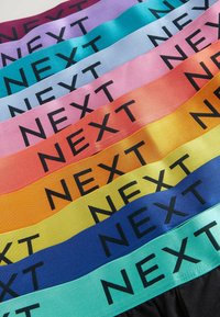 Szatén szalagok különböző színekben, fekete vastag betűkkel nyomtatva a "NEXT" felirattal. A színek között szerepel lila, gyöngyház, rózsaszín, narancs, sárga és kék.