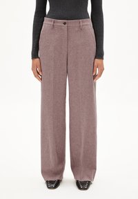 Hoge taille, wijde broek in een zachte mauve stof, met een knoopsluiting en zijzakken, gestyled met een zwart geribbeld topje en zwarte schoenen.