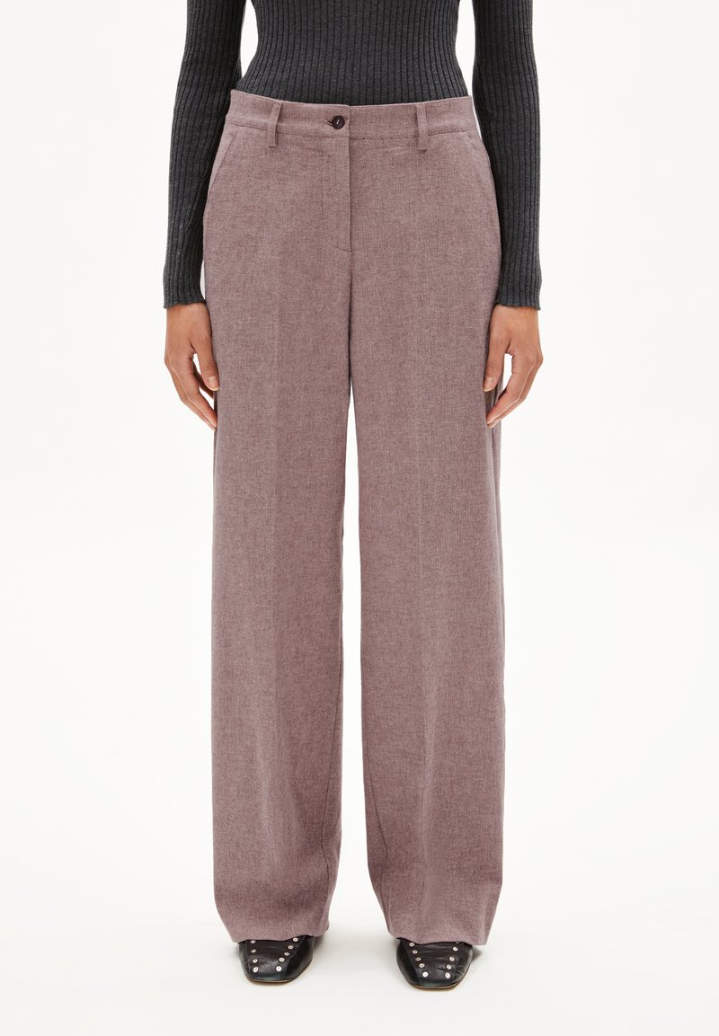 Hoge taille, wijde broek in een zachte mauve stof, met een knoopsluiting en zijzakken, gestyled met een zwart geribbeld topje en zwarte schoenen.